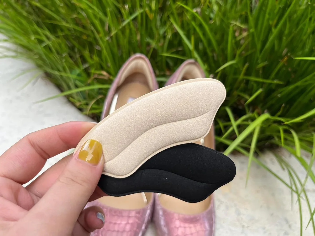 beige and black heel grips held in front of a pair of pumps