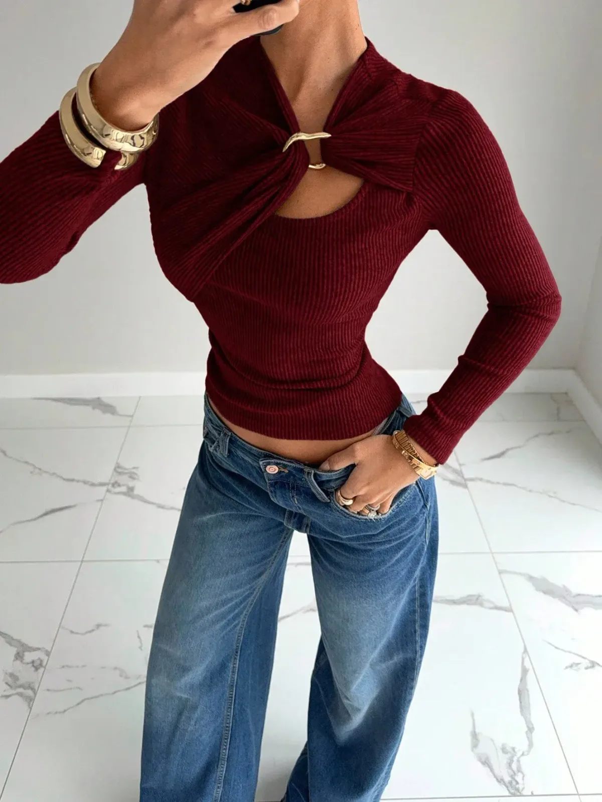 wine red cutout rib knit top tucked into jeans with gold cuffs